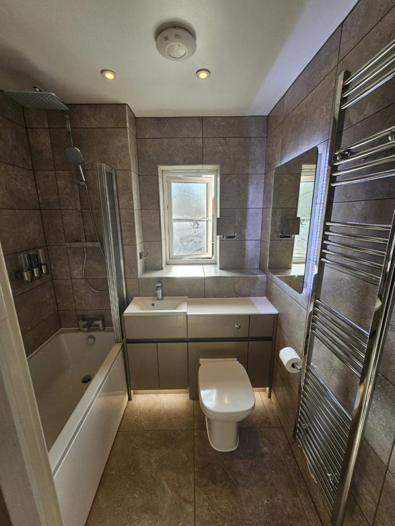 Compact bathroom with shower, sink, and storage.